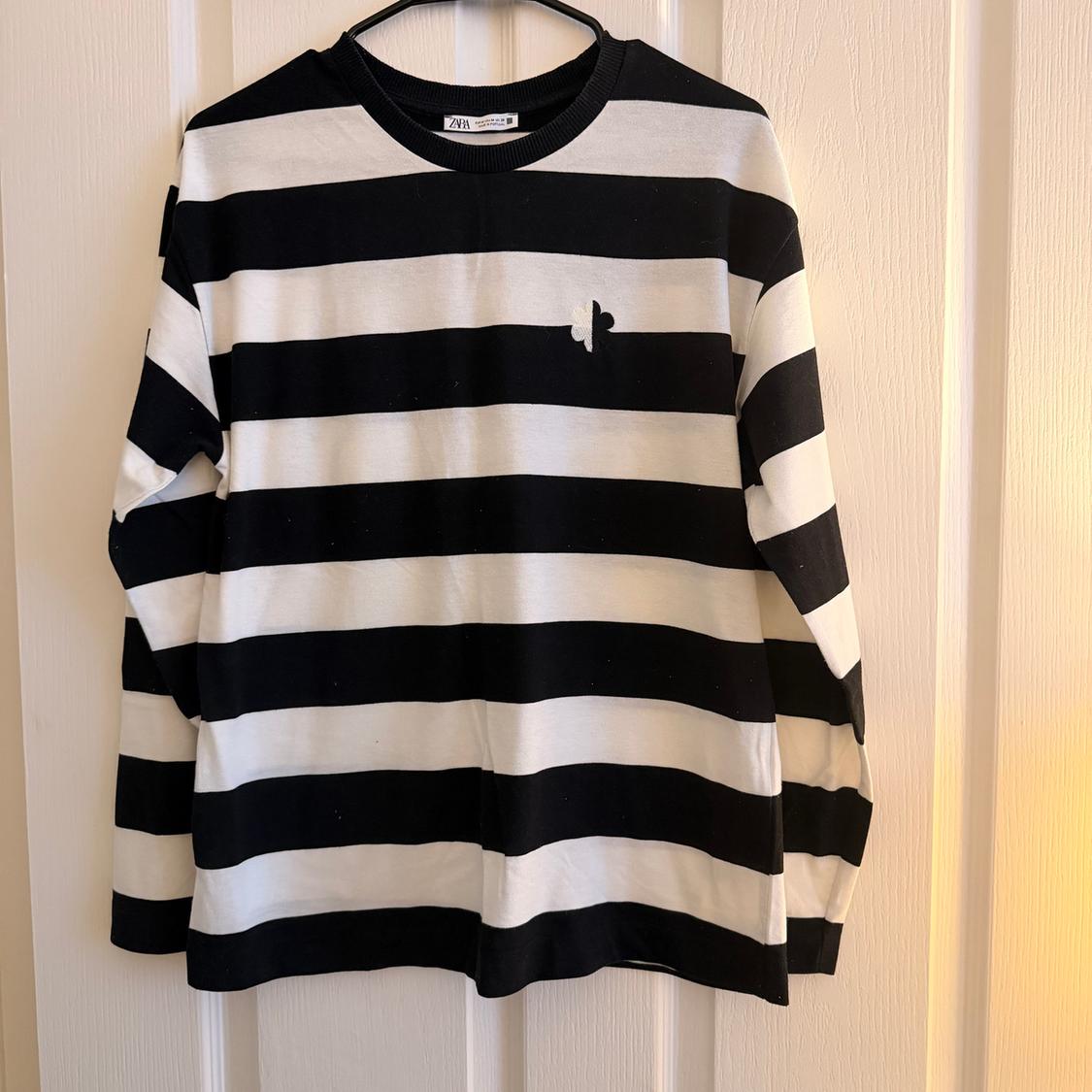 Black and white horizontal striped t-shirt hanging on a hanger. Small logo on the chest. White wall background.