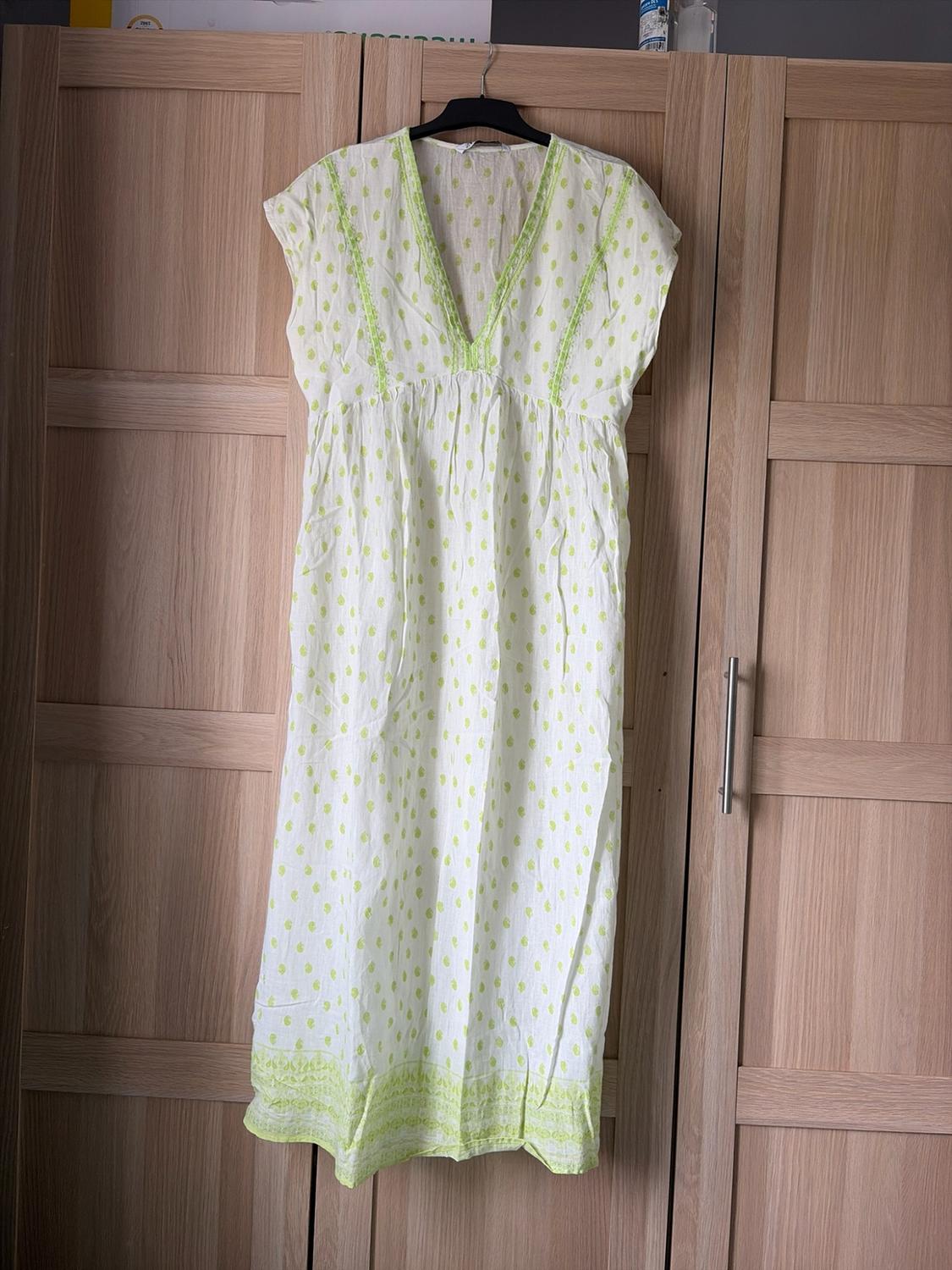 Casual white maxi dress with a light green print and V-neckline, hanging on a black hanger in front of a wooden wardrobe.