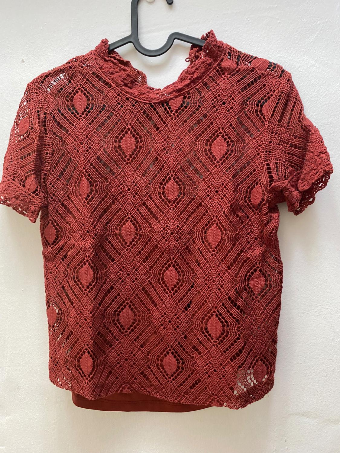 Red lace blouse with geometric design hanging on a black hanger against a white background.