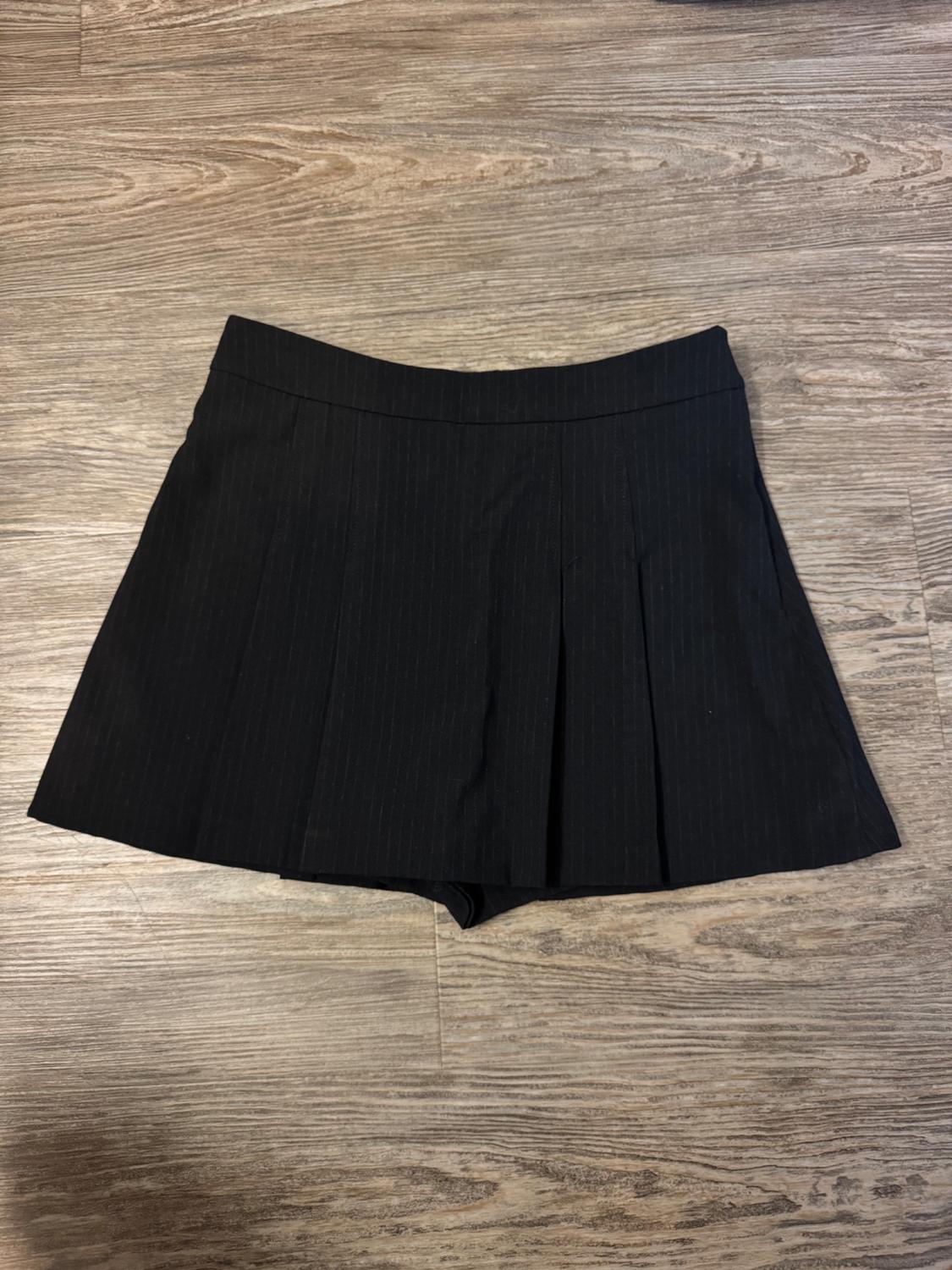 Short black pleated skirt on a light wooden floor.