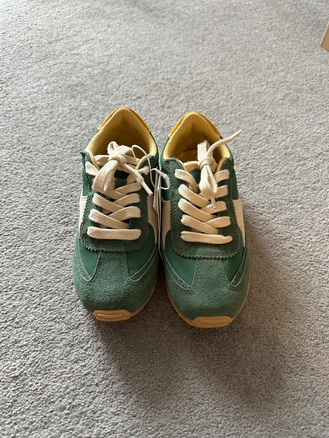 Green and beige trainers with white laces on a grey carpet. Yellow interior visible.