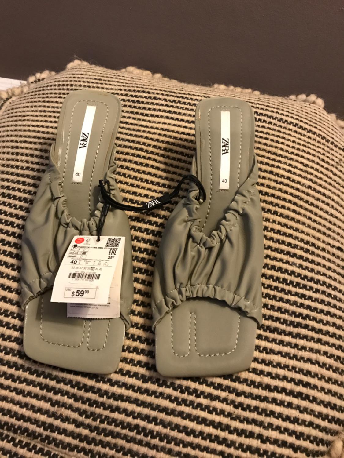 Front view of green sandals with a price tag and ruched detailing on the upper.