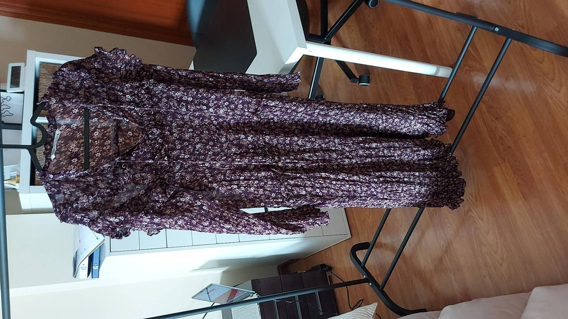 Long dress with small purple flowers hanging on a black clothes rail over a light wooden floor.