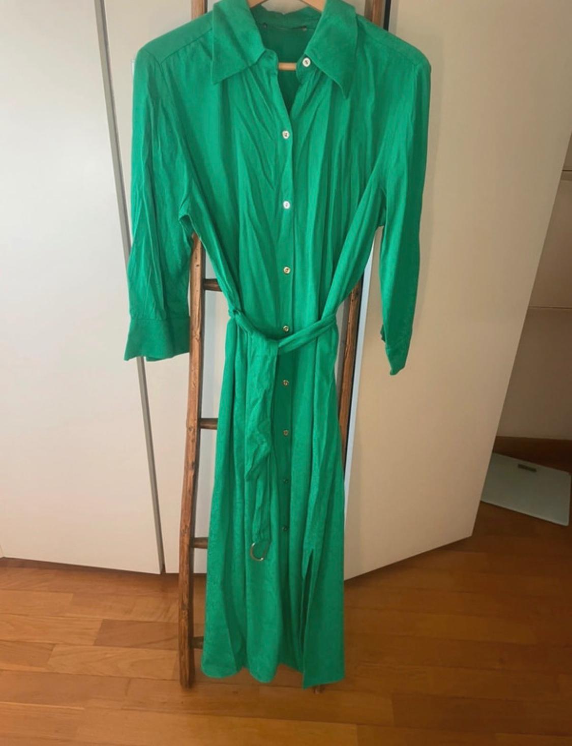 Long green shirt dress with buttons and a belt, hanging on a wooden ladder in a room with a wooden floor.