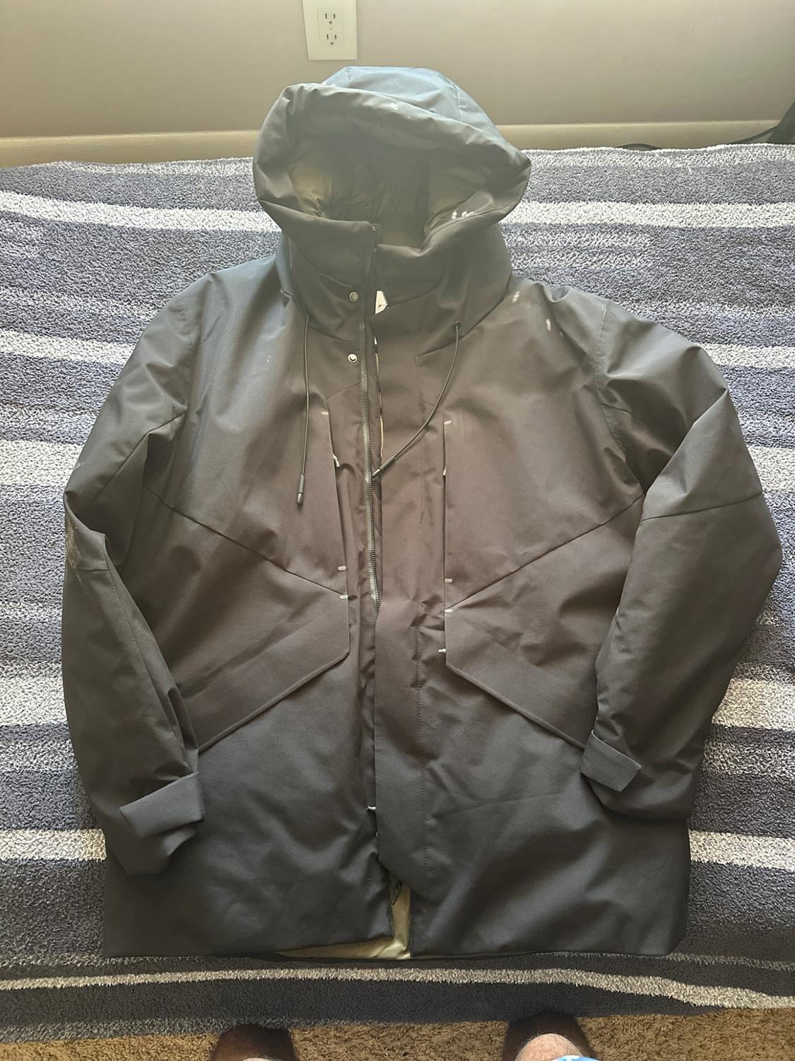 Black hooded coat draped over a striped blanket.  
Design with a front zipper and drawstrings.