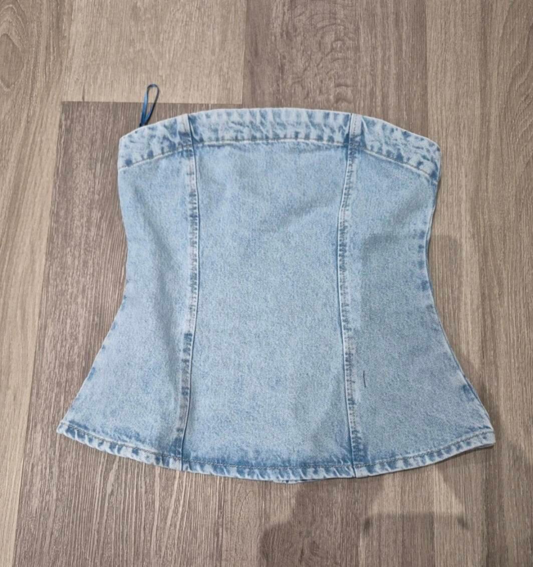 Light blue denim corset on a wooden floor. Fitted design with visible vertical seams.