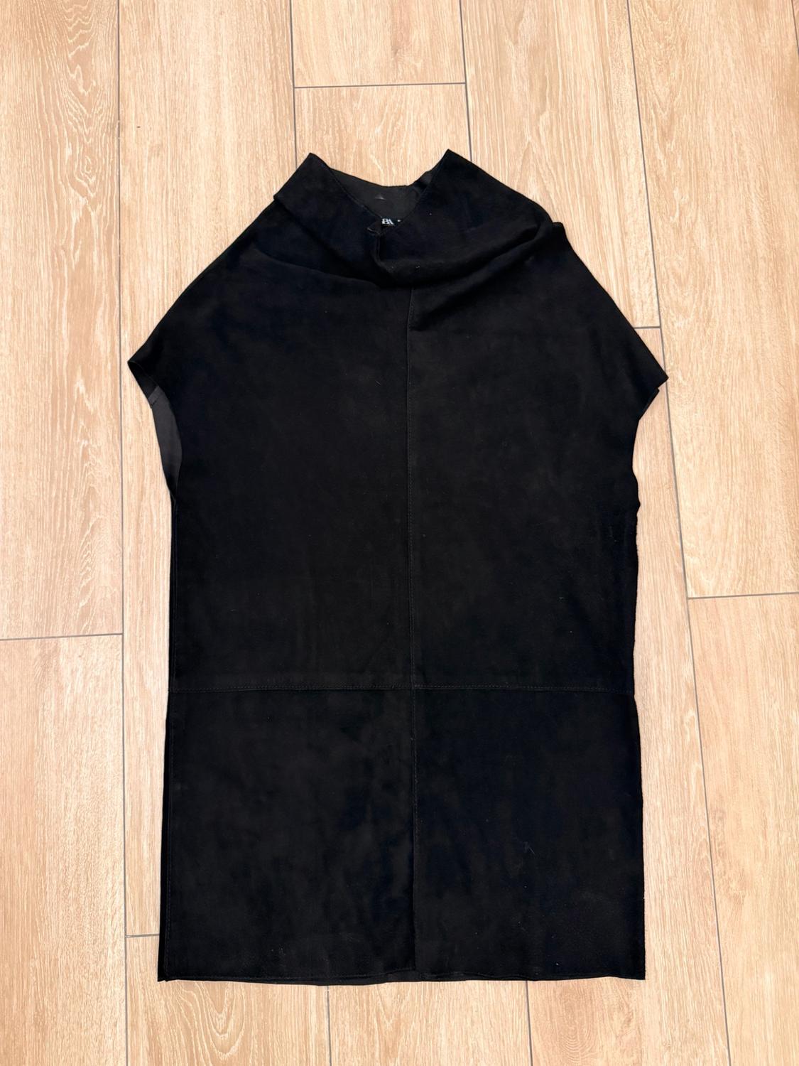 Black sleeveless, high-neck top with central and horizontal seams, on a wooden floor.