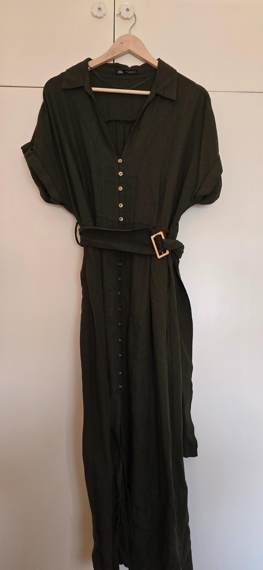 Dark green short-sleeved shirt dress with buttons and a belt, hanging on a wooden hanger against a white background. Text: ZARA.