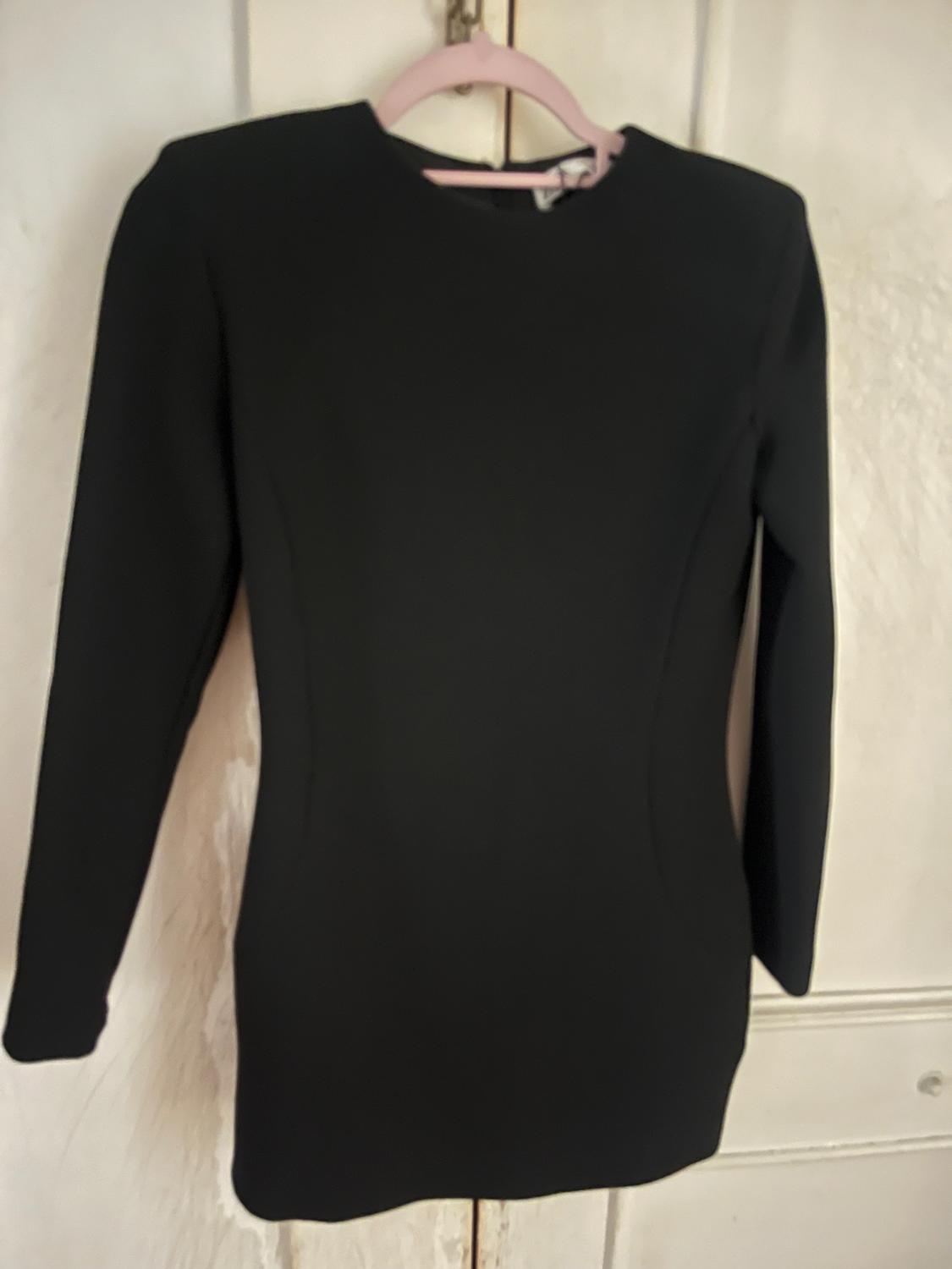 Long-sleeved black dress hanging on a pink hanger over a white door. Simple and elegant design.