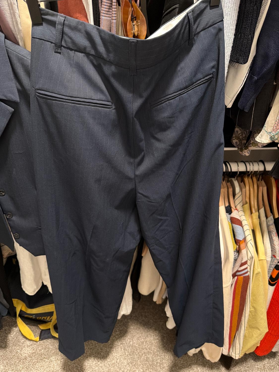 Dark blue pants hanging in a closet, surrounded by other garments of various colors. Background of sweaters and jackets.