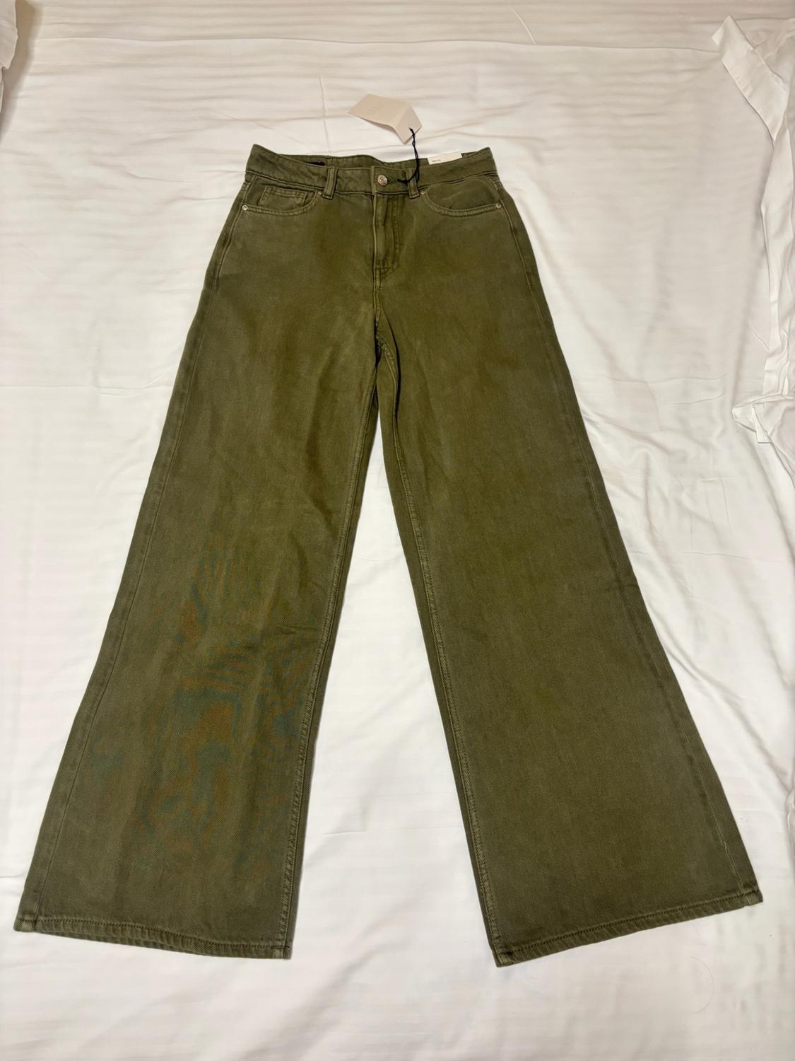 Olive green wide-leg jeans with tags on, laid out on a creased white sheet.