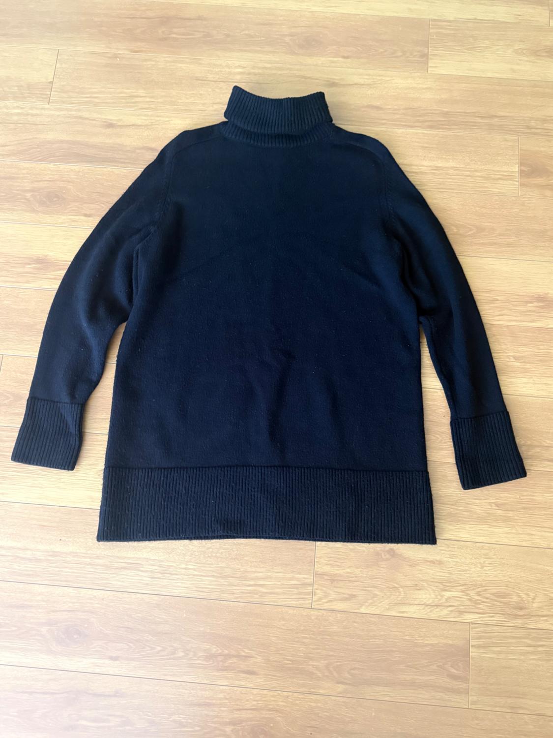 Black roll-neck, long-sleeved jumper on a light wooden floor.