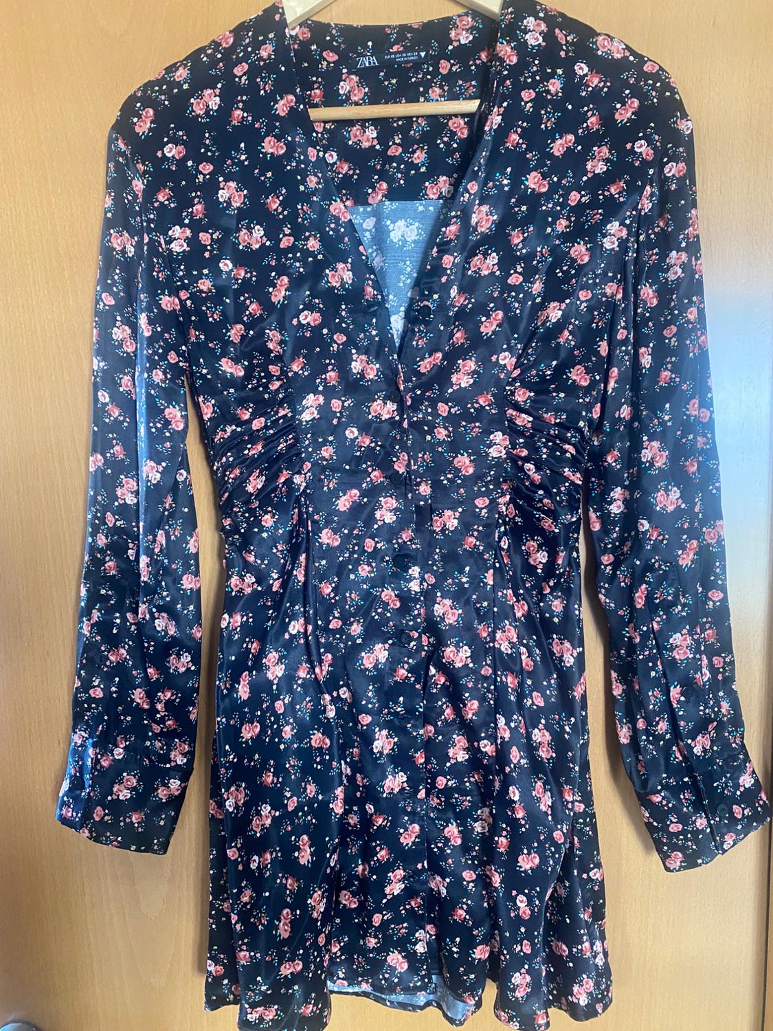 Long-sleeved dress with a pink-toned floral print and a dark background, hanging on a wooden hanger.