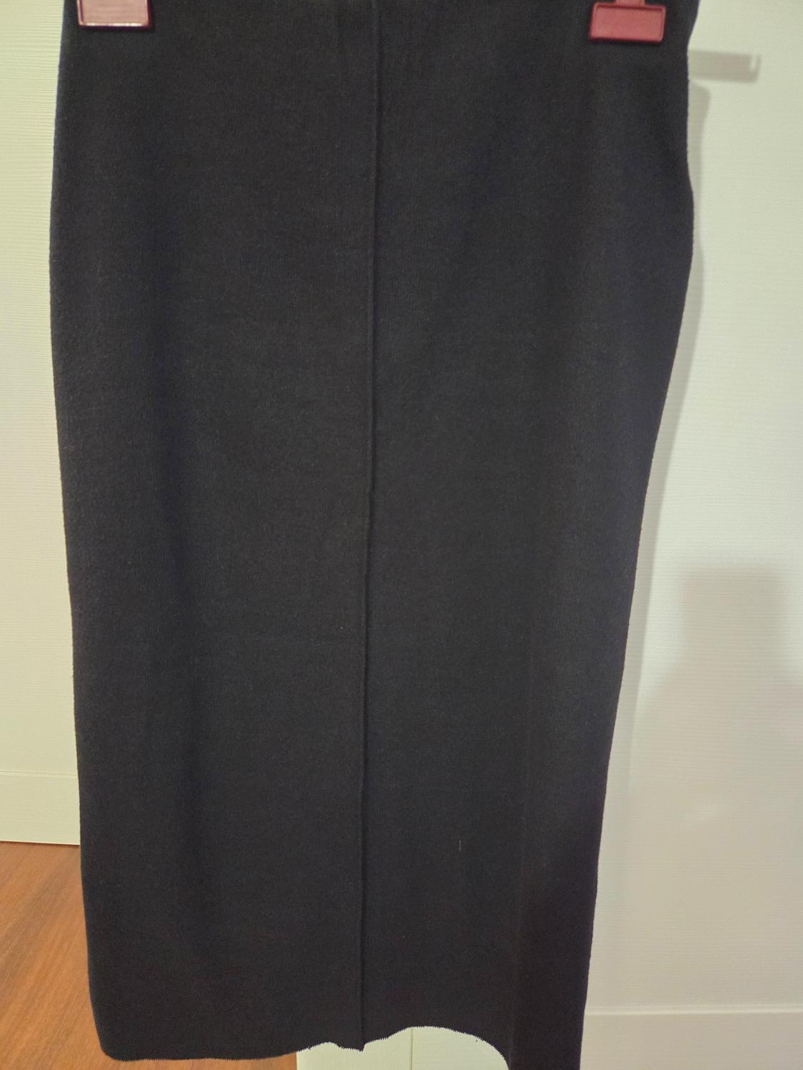 Black skirt hanging on a hanger with red clips, against a white background and wooden floor.
