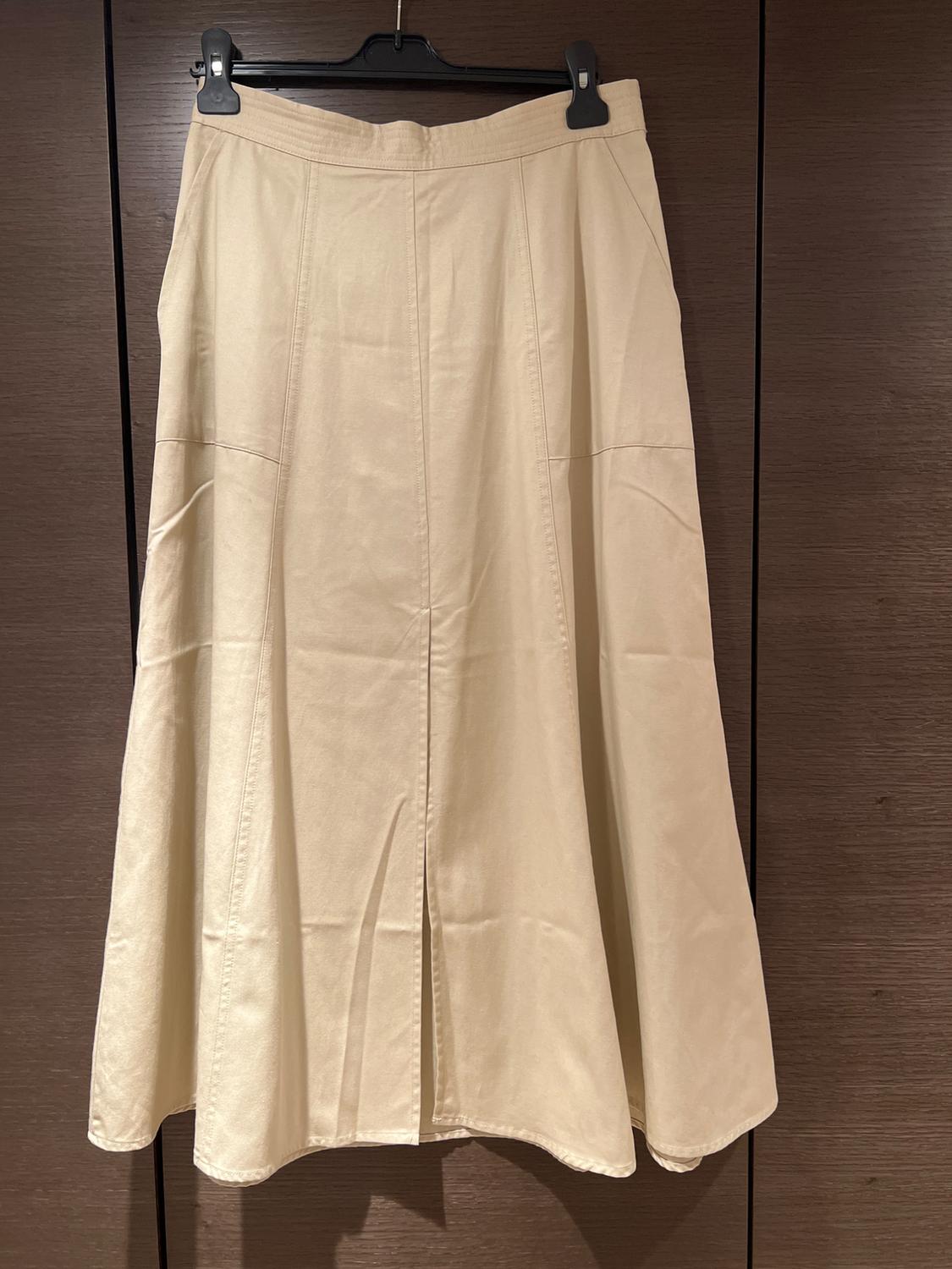 Long beige skirt with vertical seams hanging on a black hanger in front of a dark wooden wardrobe.