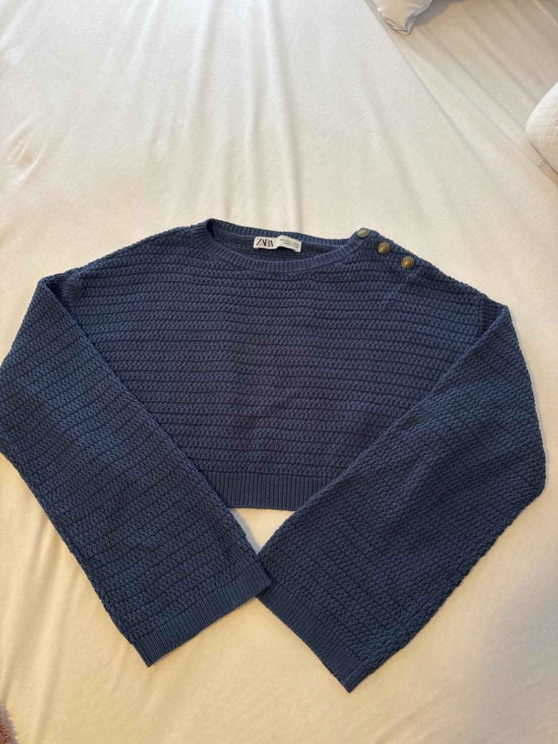 Navy blue short knit jumper with a round neck, wide sleeves and button detail on the shoulder. ZARA label. Laid out flat on a white sheet.