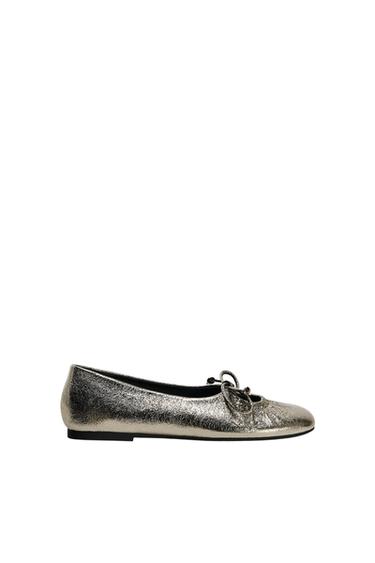 Silver metallic ballerina flat with decorative bow on top, black flat sole, on white background.