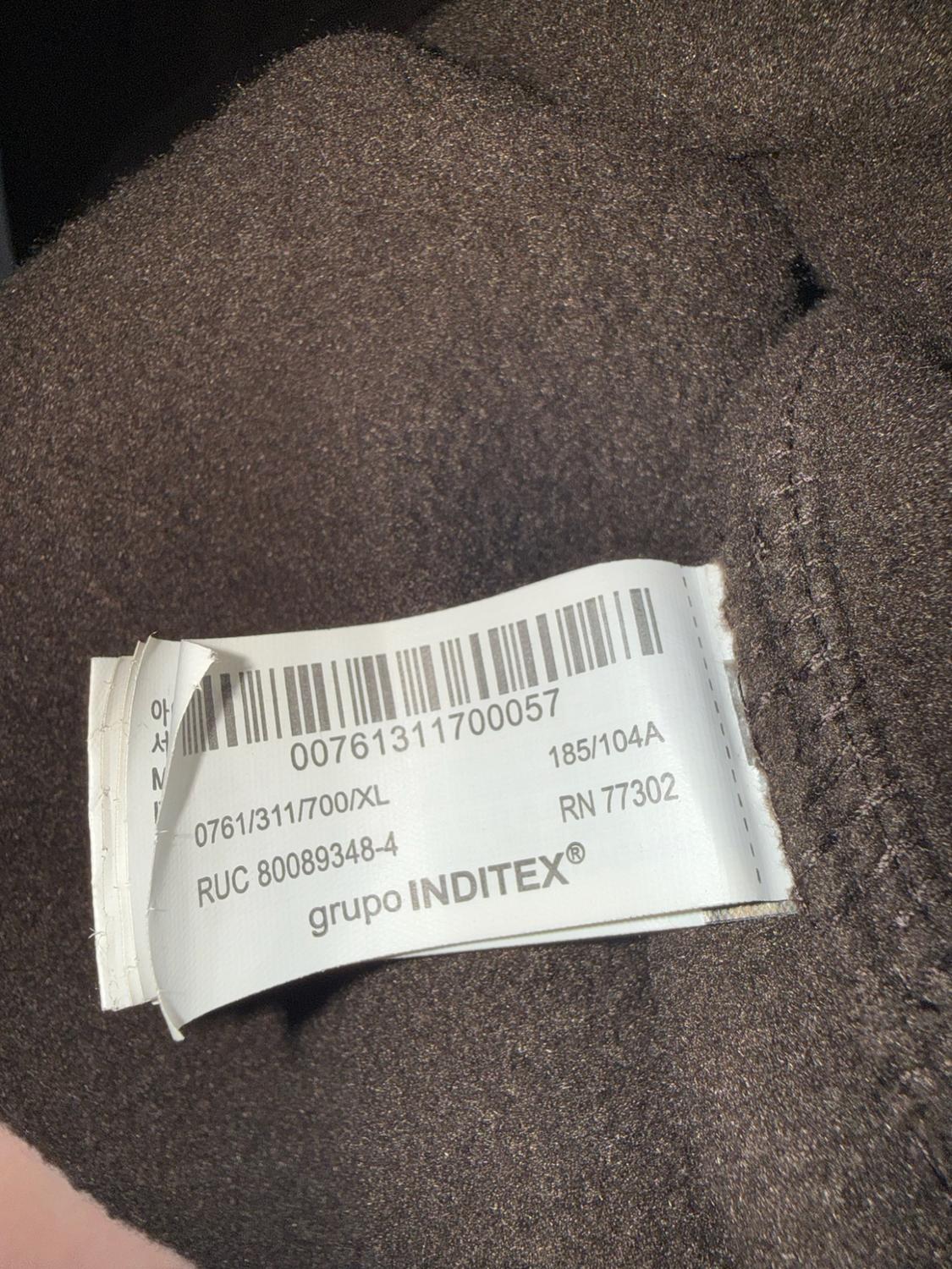 White label on brown fabric. Text: 00761311700057, 0761/311/700/XL, 185/104A, RUC 80089348-4, RN 77302, INDITEX® group.