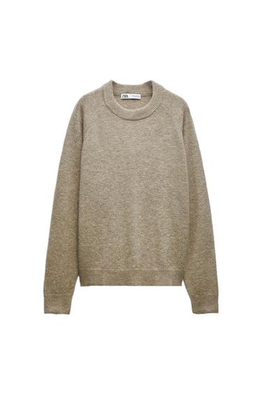 Beige knit sweater with a crew neck and long sleeves. Ribbed cuffs and hem. Visible ZARA label on the inside. White background.