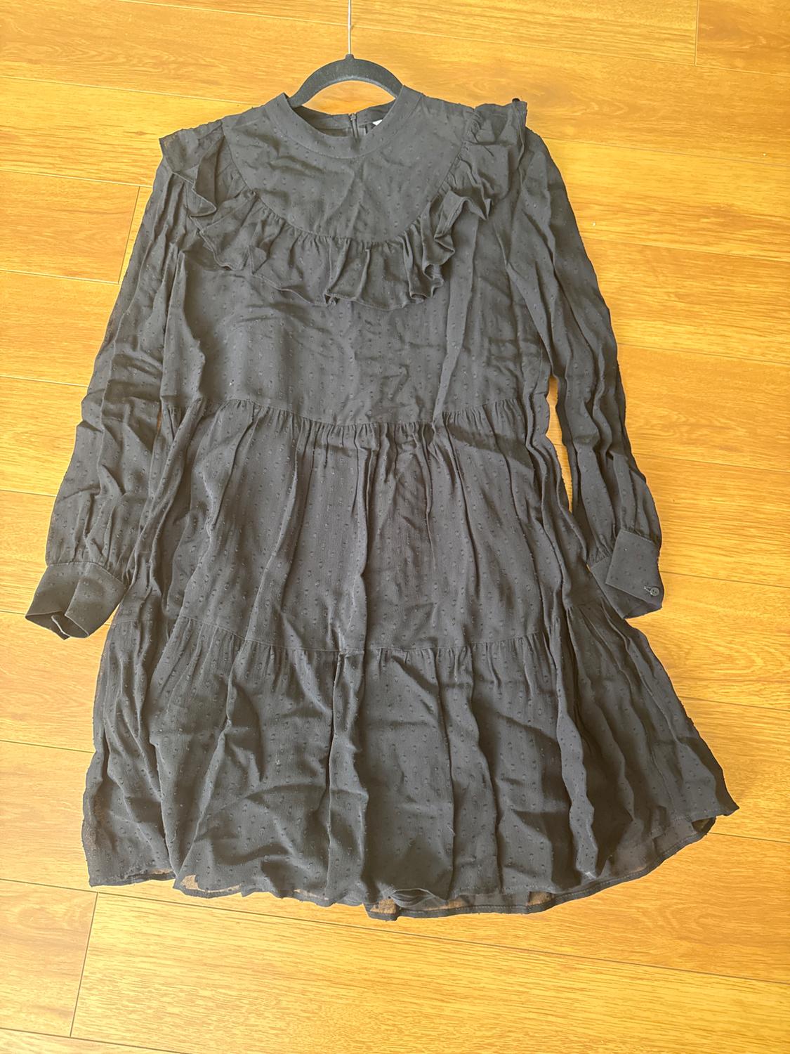 Long-sleeved black dress with ruffles on the chest and a flared skirt, hanging over a light wooden floor.