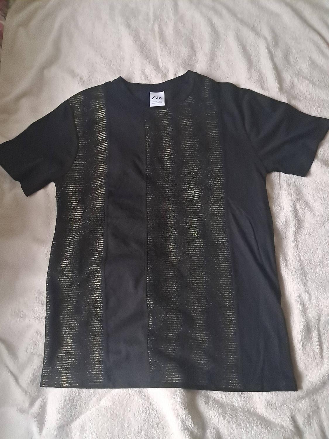 Black short-sleeved T-shirt with gold vertical stripes, laid flat on a light-coloured surface. Label with the text ZARA.