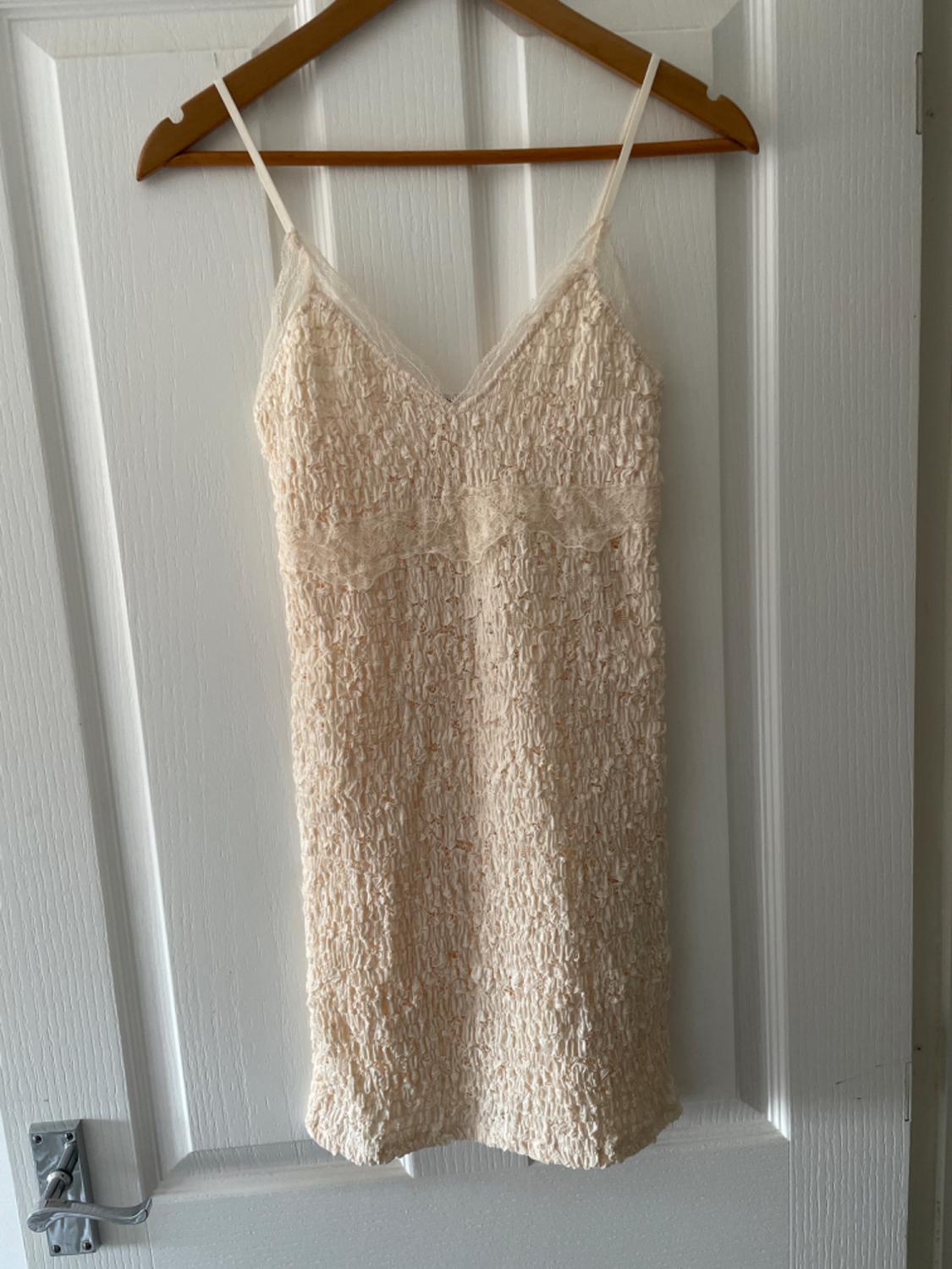 Cream textured slip dress with spaghetti straps and lace, hanging on a wooden hanger over a white door.