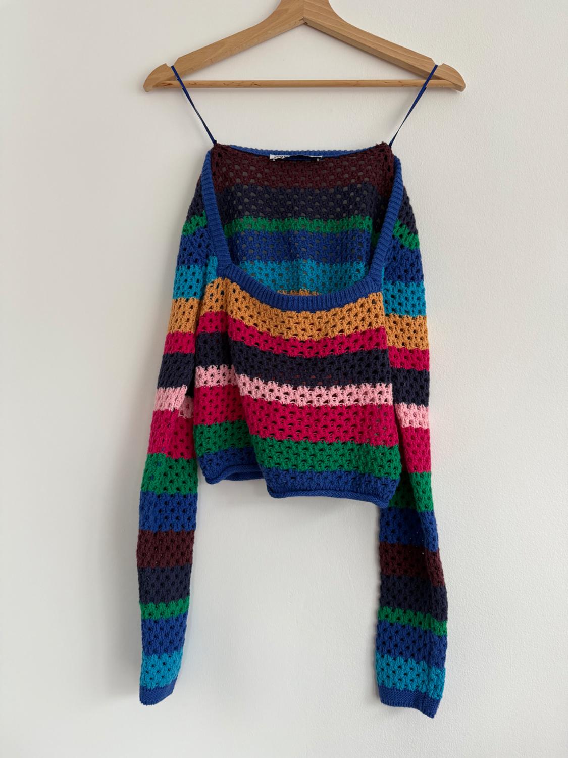 Multi-coloured crochet jumper with horizontal stripes in blue, green, pink and brown, hanging on a wooden coat hanger.