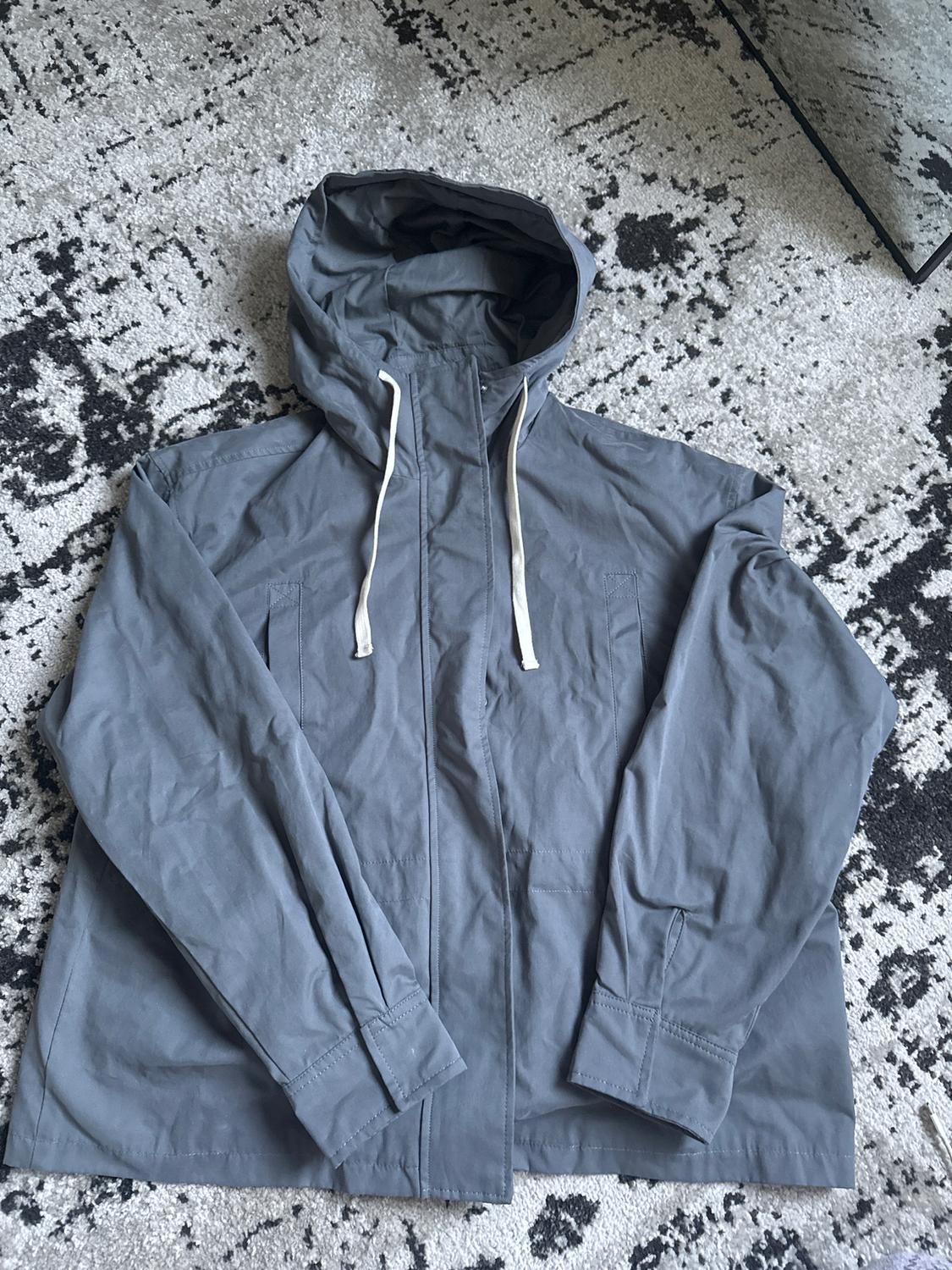 Grey hooded jacket with white drawstrings, on an abstract design rug in shades of grey and black.