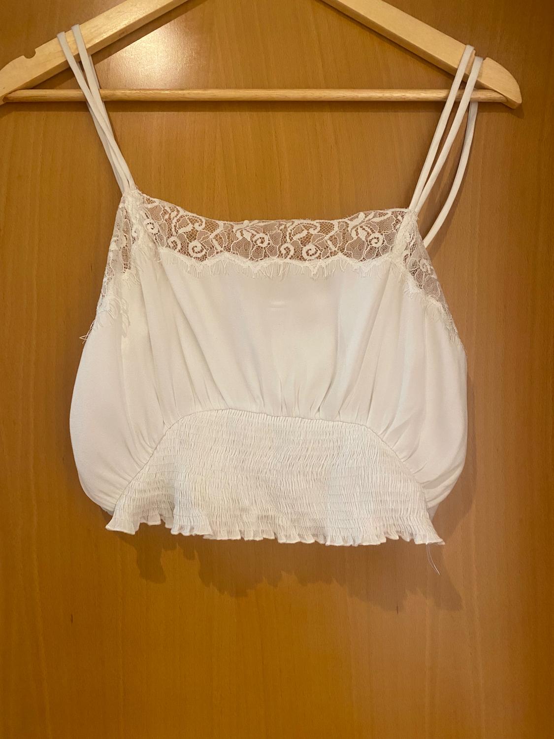 White top with spaghetti straps and lace trim at the neckline, hanging on a wooden hanger against a light wood background.