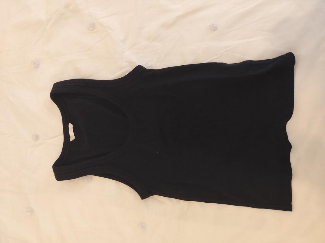 Black sleeveless top on a white surface with small circular details.