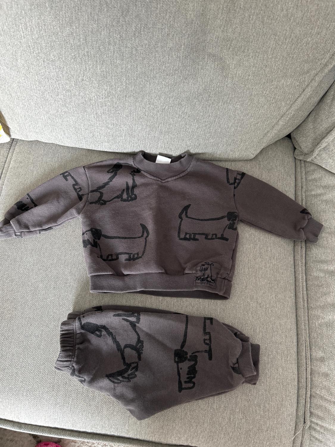 Grey children's set with black dachshund print, consisting of a sweatshirt and trousers, on a light grey sofa.