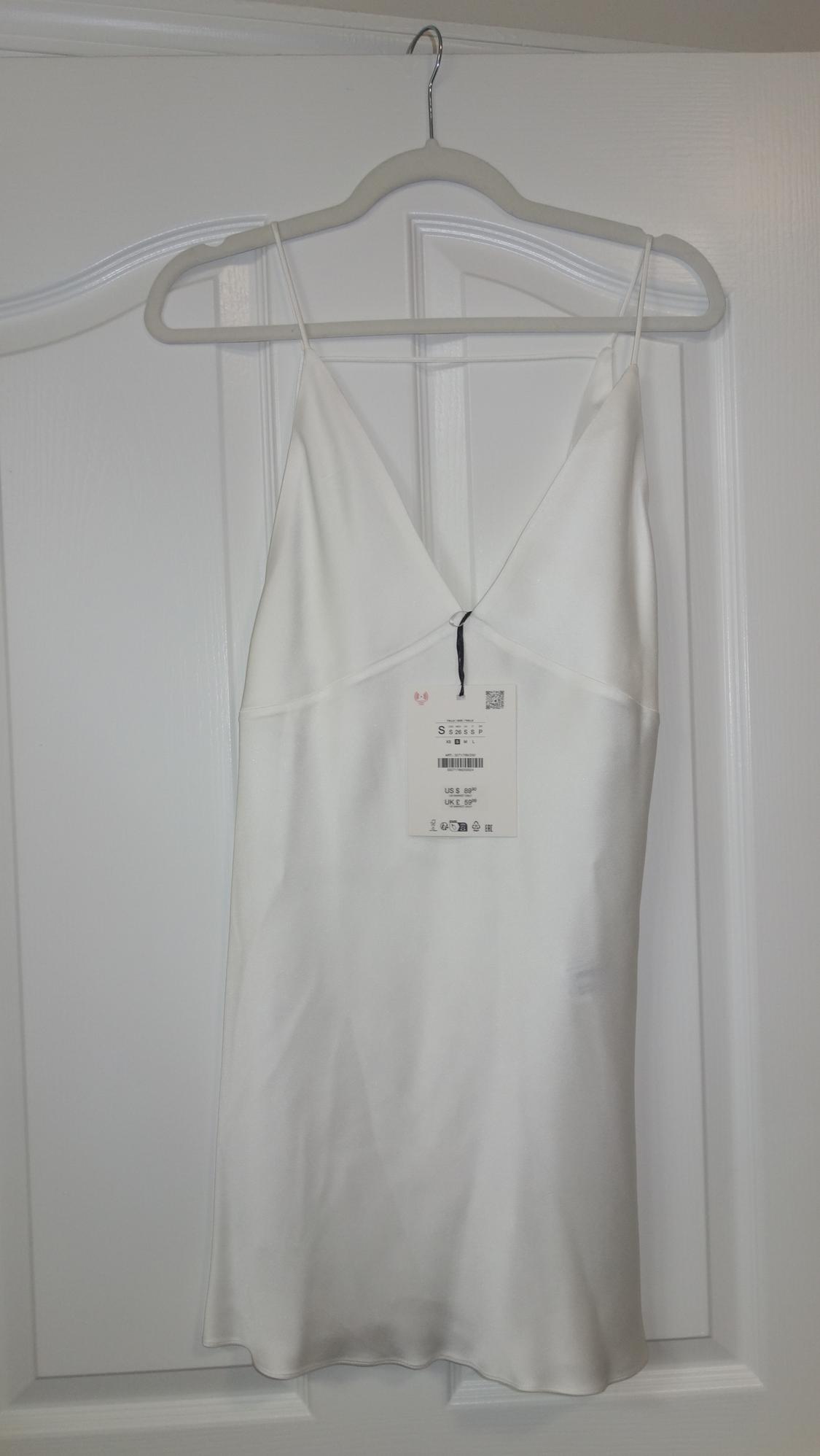 White spaghetti strap tank top hanging on a white hanger over a door. Visible tag with product details.