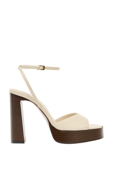 Side view of a beige sandal with a high heel and adjustable strap.