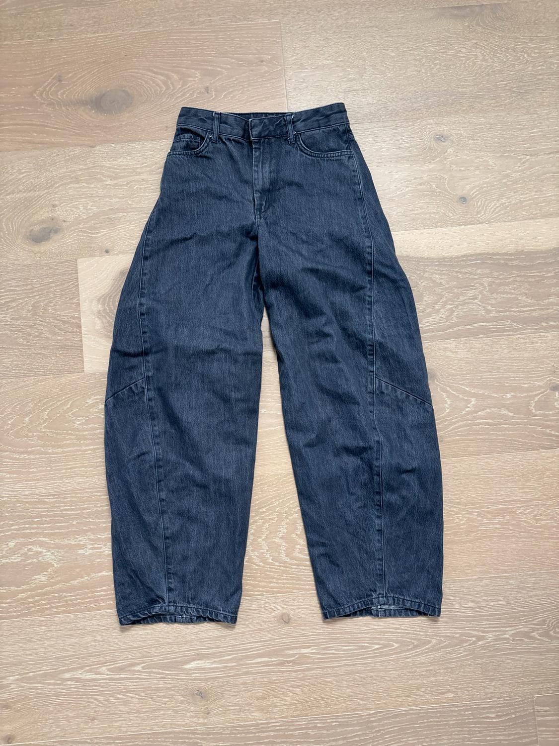 High-waisted gray dark denim pants with a wide cut and a rounded silhouette, on a light wood floor.