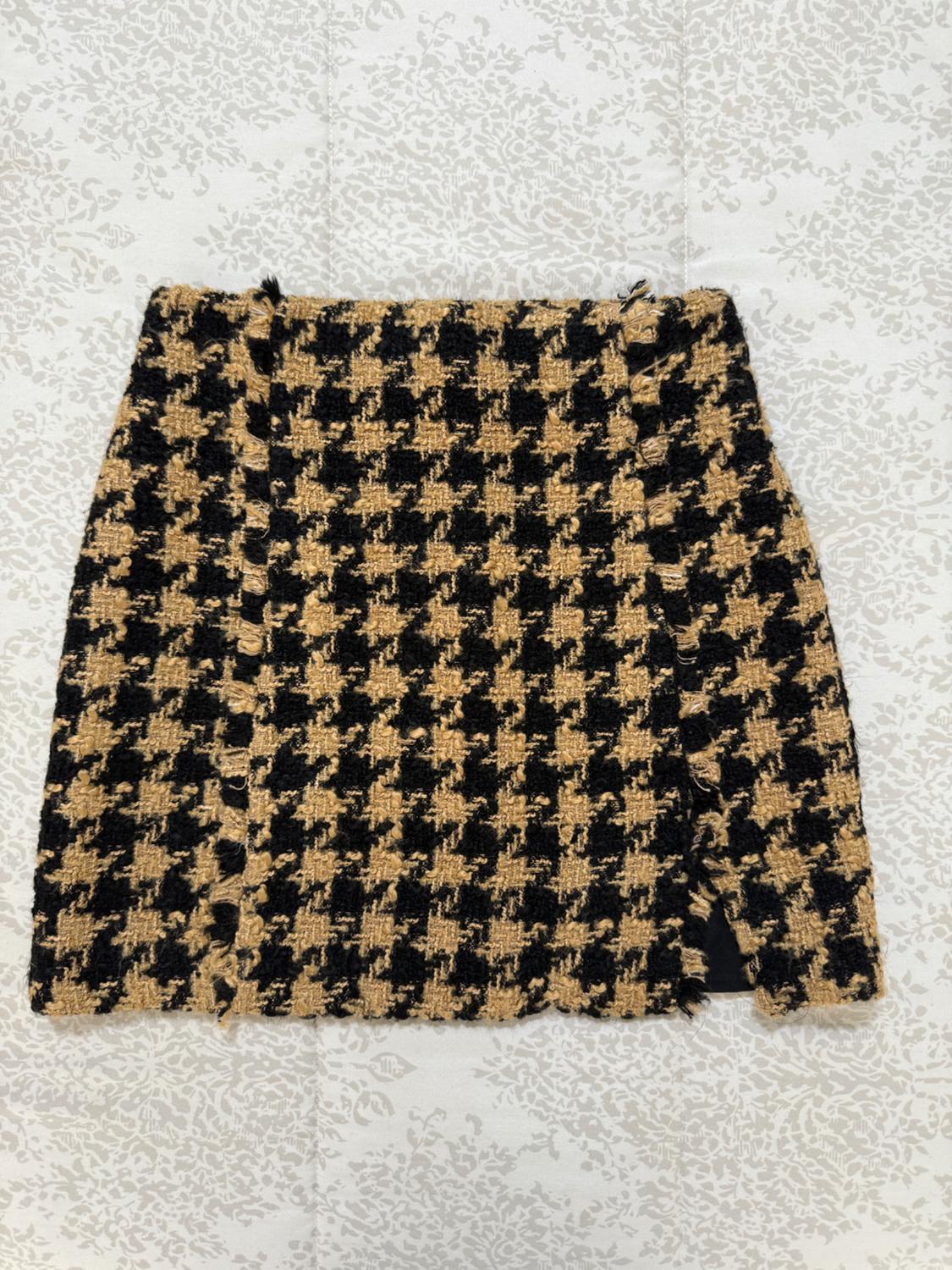 Front view of a short black and beige houndstooth print skirt.