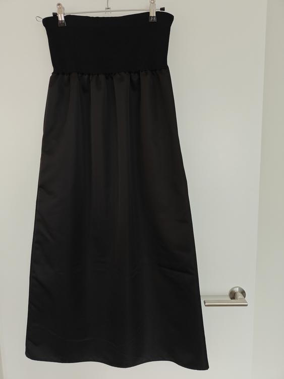 Black long skirt hanging on a hanger over a white door. The top part is elasticated and the fabric is smooth and shiny.