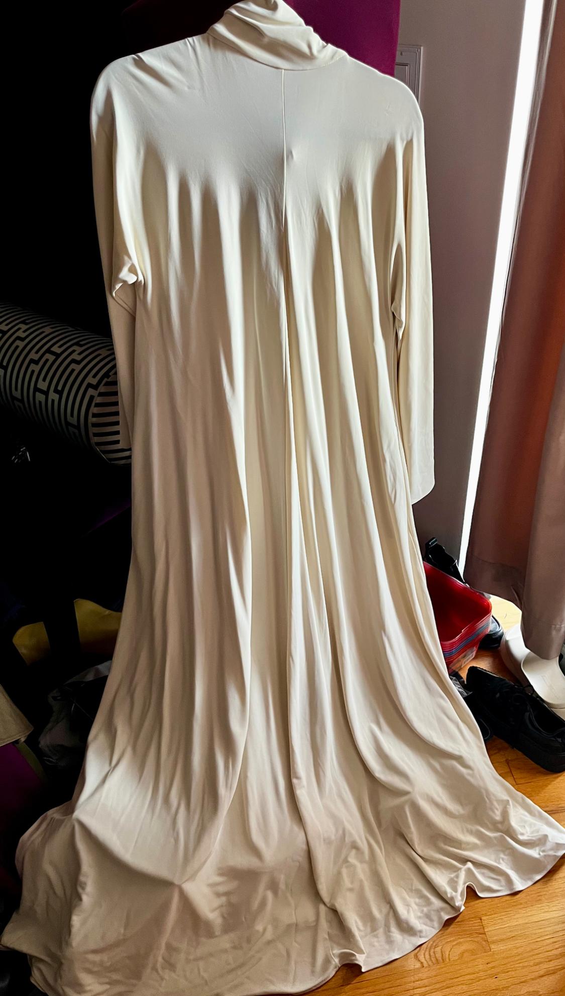 Cream-coloured maxi dress draped over a chair, with a dark backdrop and details of shoes and curtains surrounding it.