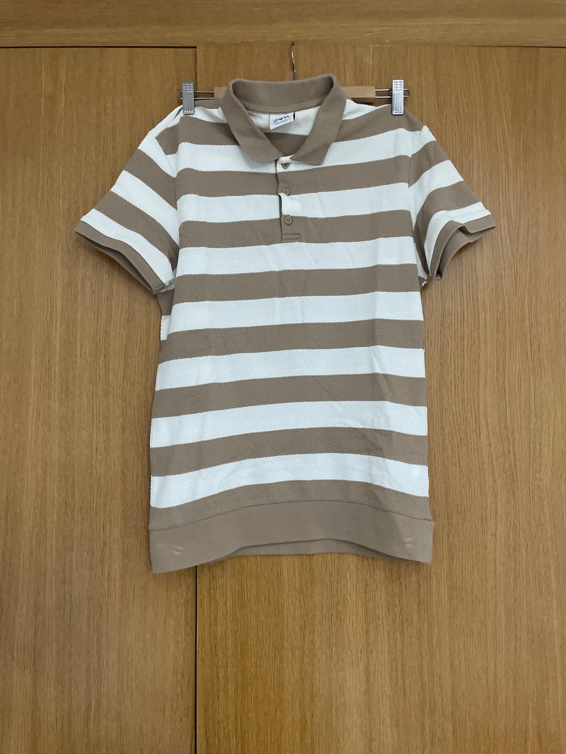 Beige and white horizontal striped polo shirt hanging on a wooden door.