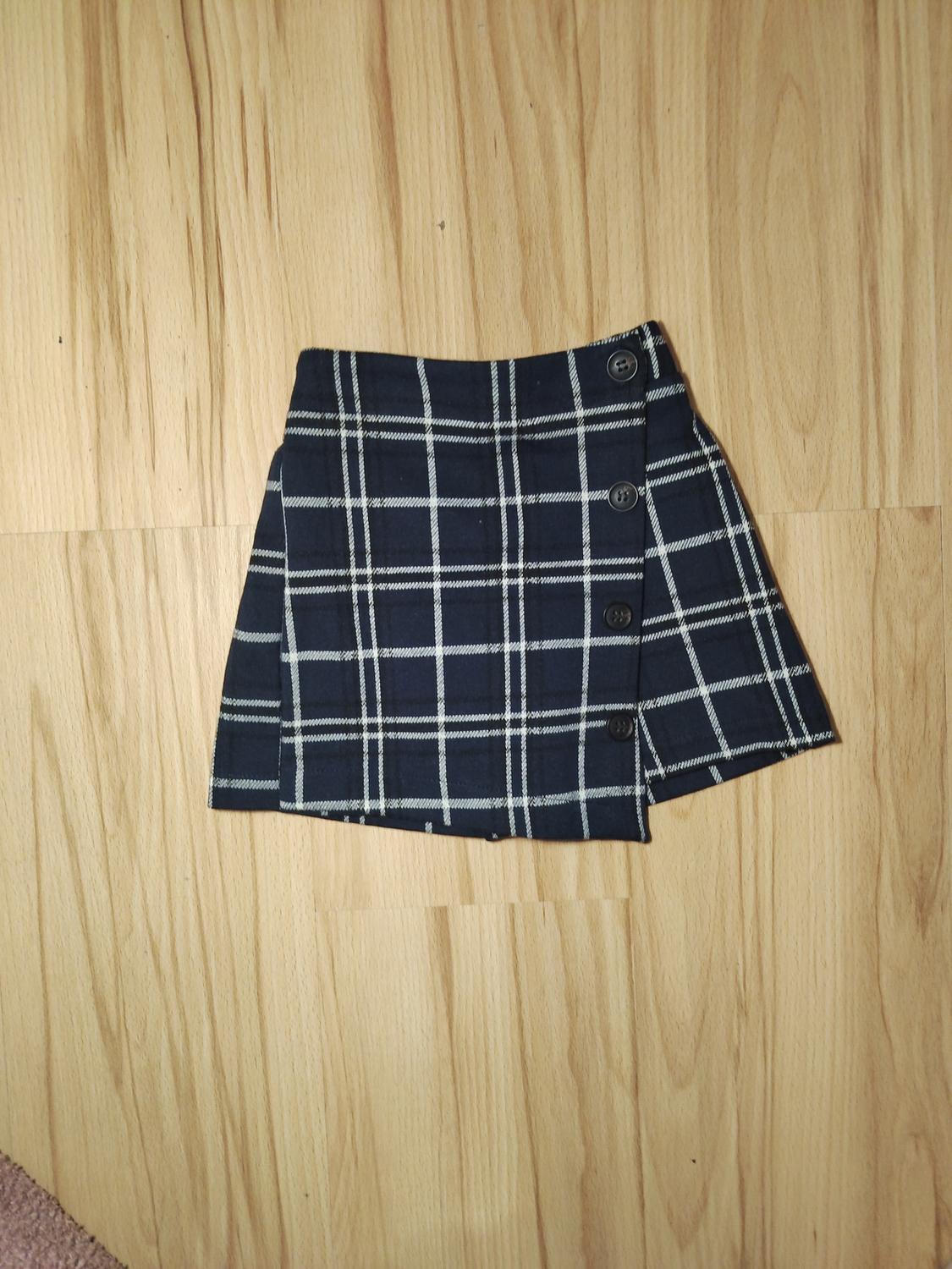 Black and white checked mini skirt with buttons on the side, on a light wooden floor.
