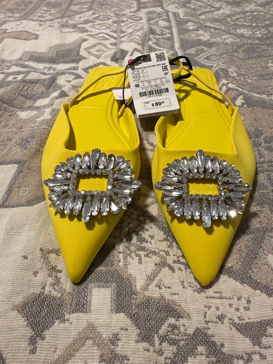 Pointy yellow shoes with rhinestone embellishments on the upper, on a printed fabric. Visible price tag: $89.90.