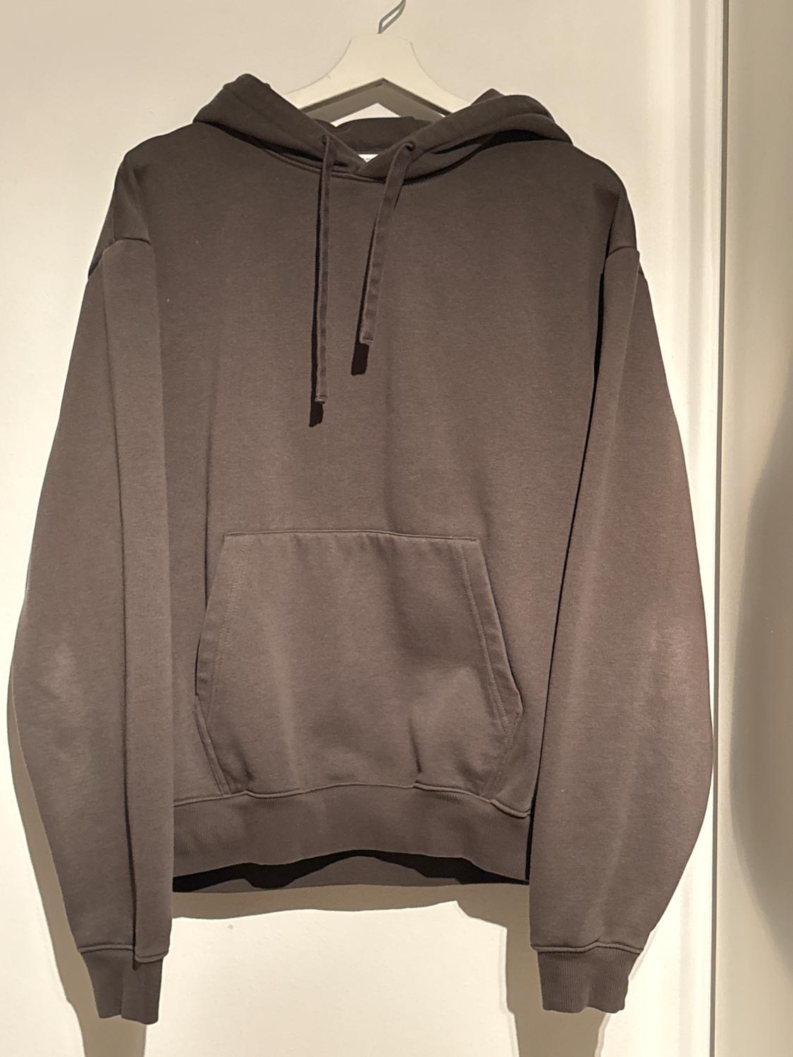 Brown hooded sweatshirt with a front pocket, hanging on a white hanger against a light background.