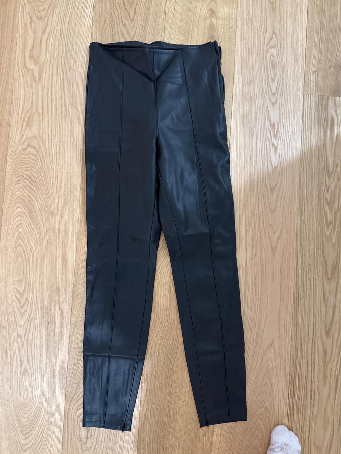 Black synthetic trousers on a light wooden floor. Part of a foot in a white sock visible in the bottom right corner.