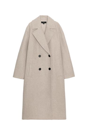 Front view of a long beige coat with wide lapels, black double-breasted fastening and side pockets.