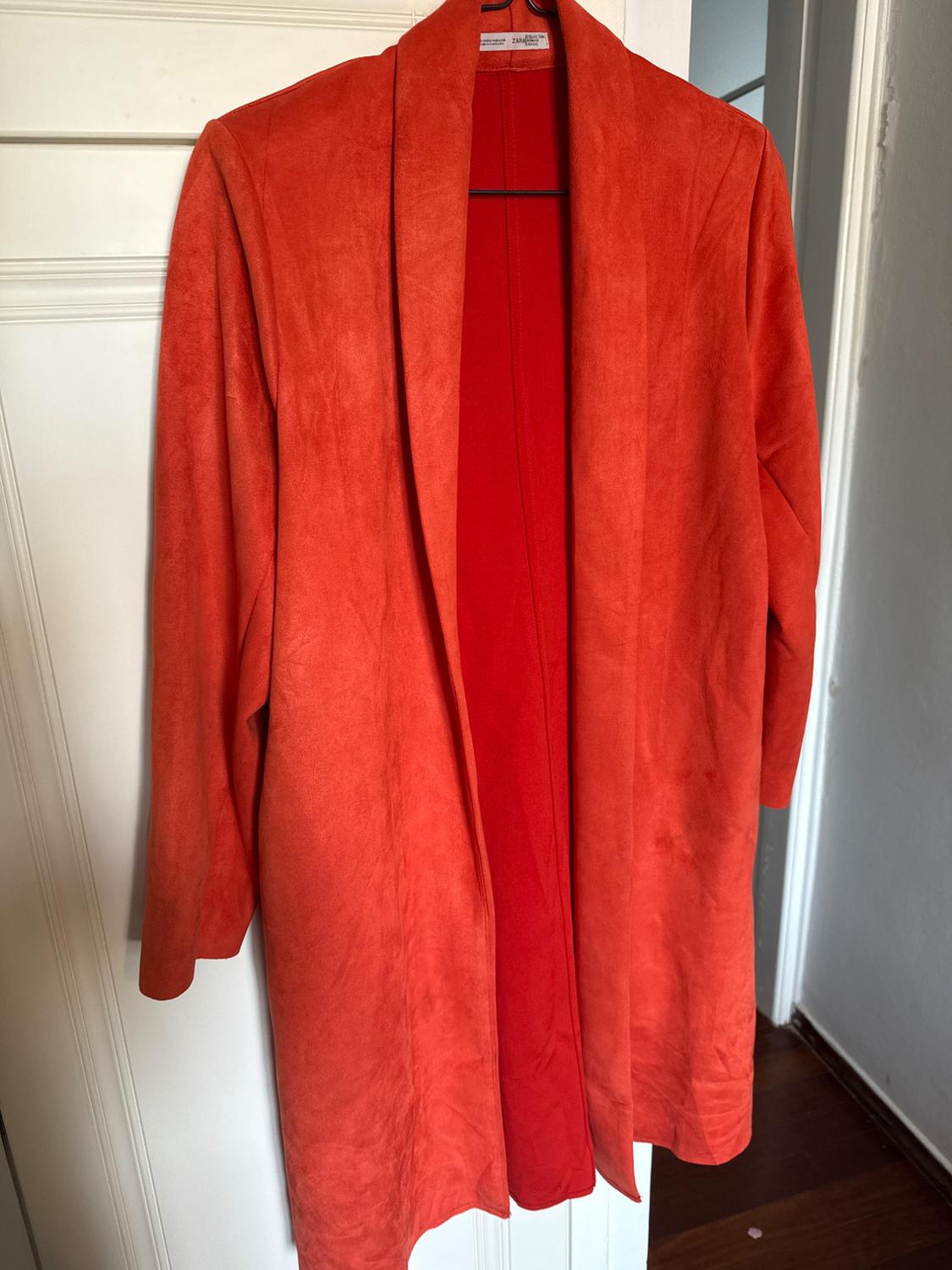 Long orange coat hanging on a white door. The coat has a simple design with no visible buttons.