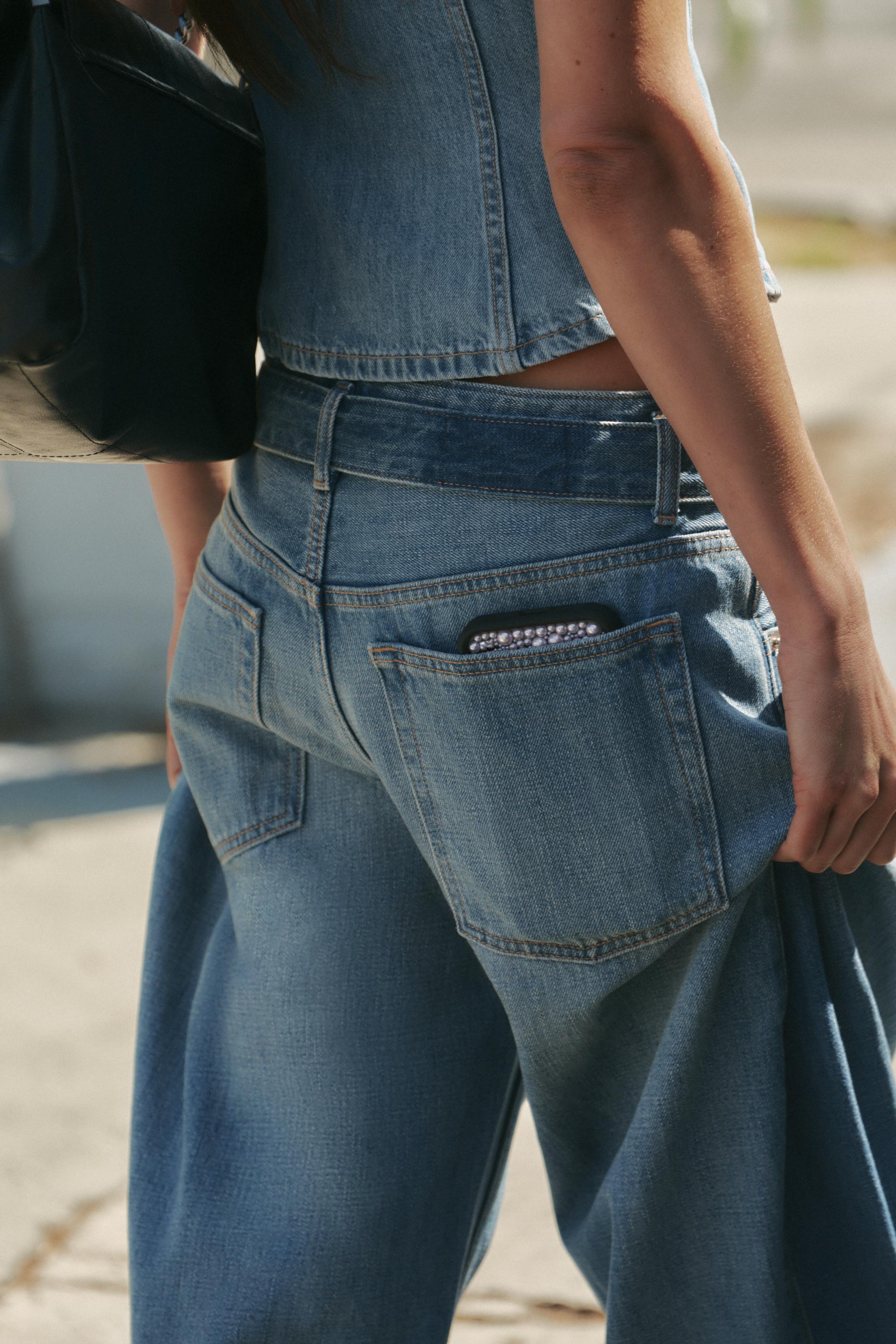 Medium shot of blue jeans with visible back pockets, one with a decorated phone.