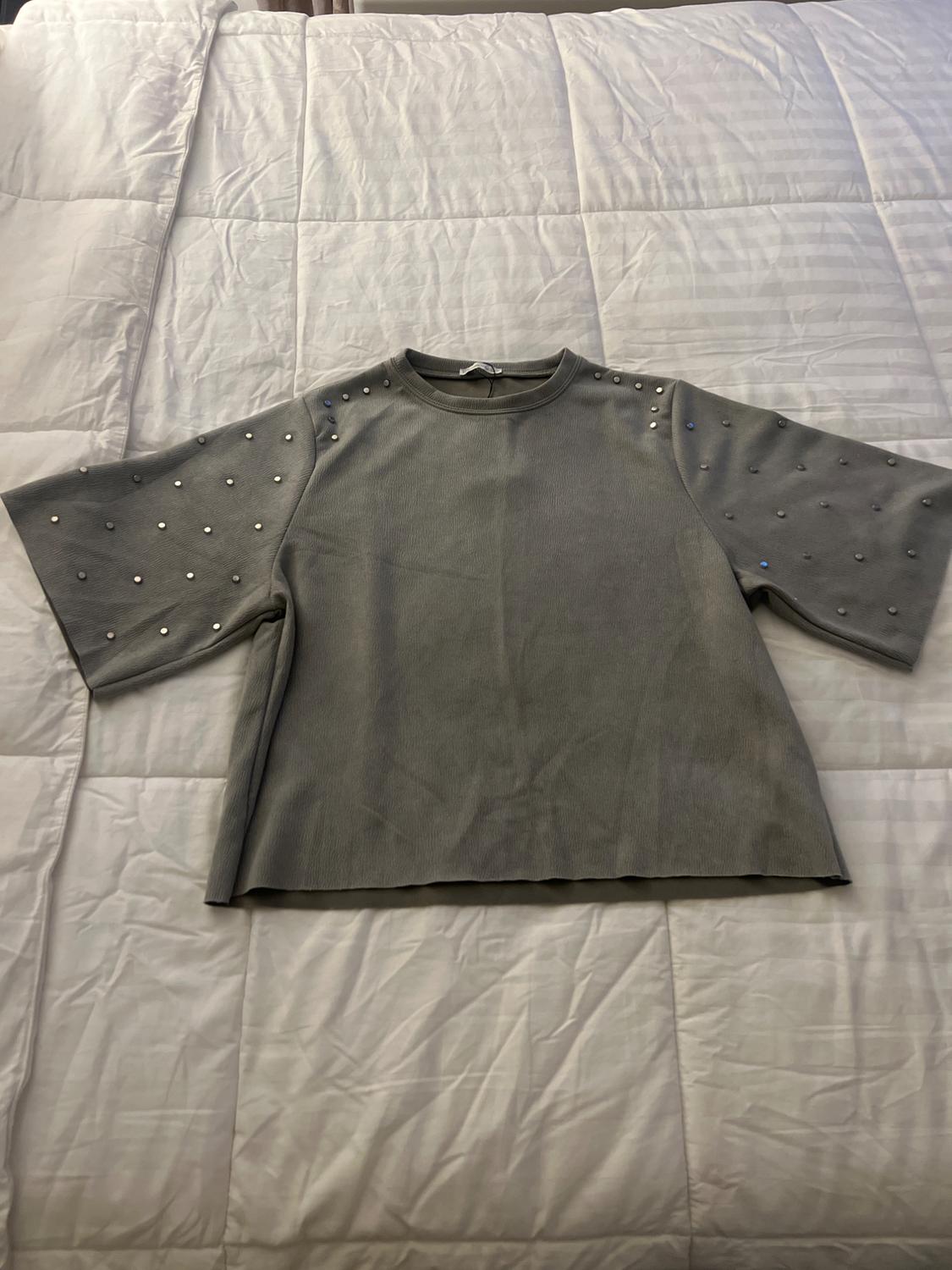 Front view of a grey blouse with short sleeves and stud details on the shoulders and sleeves.