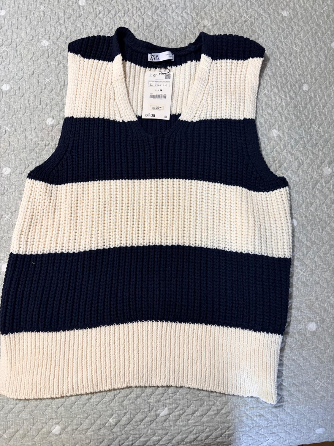 Black and white striped knit vest on a gray surface with visible price tag.