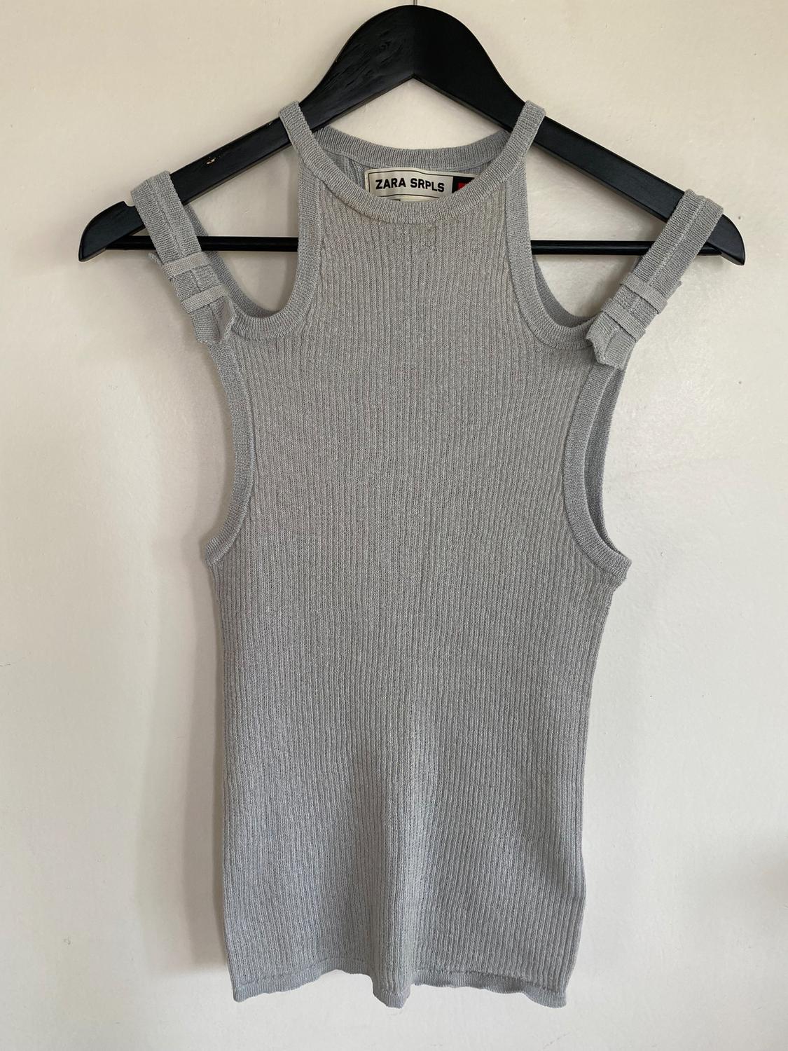 Gray sleeveless ribbed knit top hanging on a black hanger. Visible tag: "ZARA SRPLS". White background.