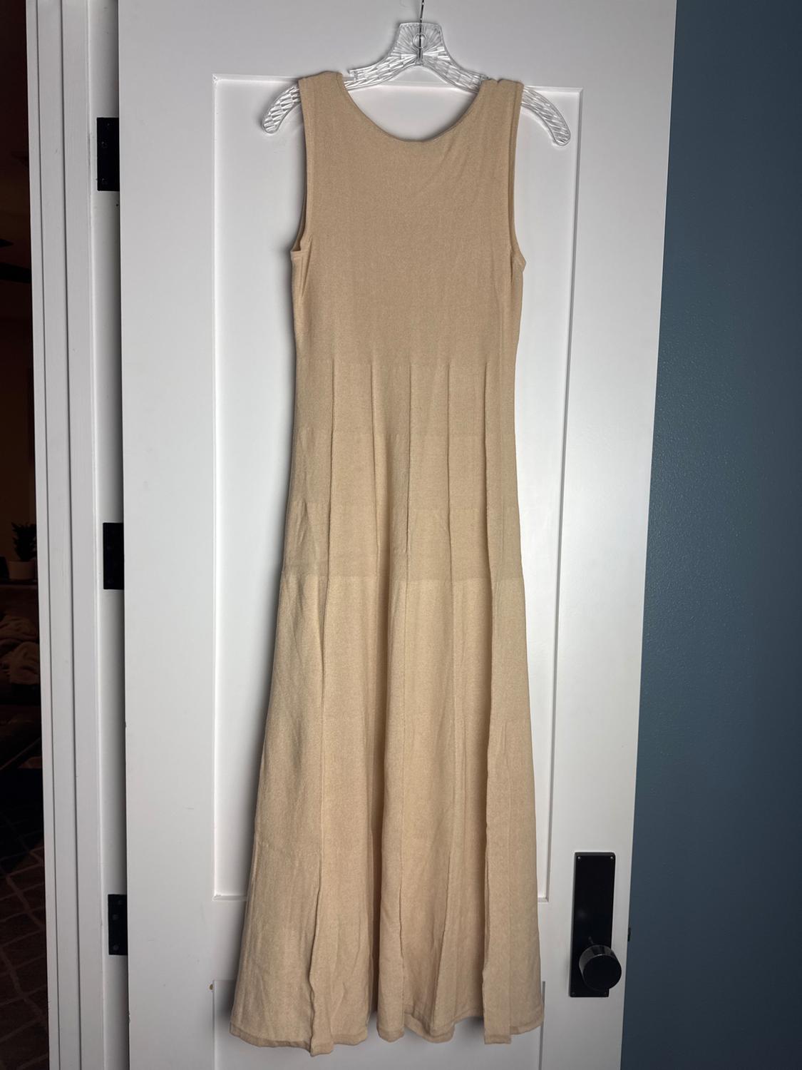 Beige sleeveless knitted maxi dress, hanging on a hanger over a white door in a casual home setting.