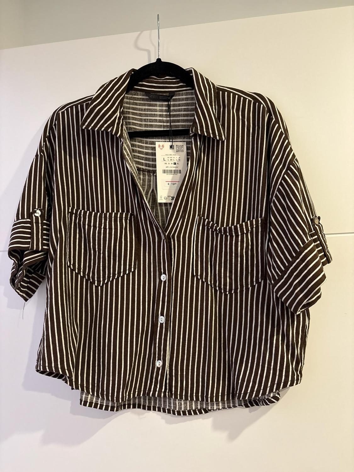 Dark and white vertically striped shirt on a hanger. Short sleeves, two pockets and a label reading ZARA L €19.95.